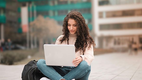 Jovem sentada ao ar livre a trabalhar num computador portátil.